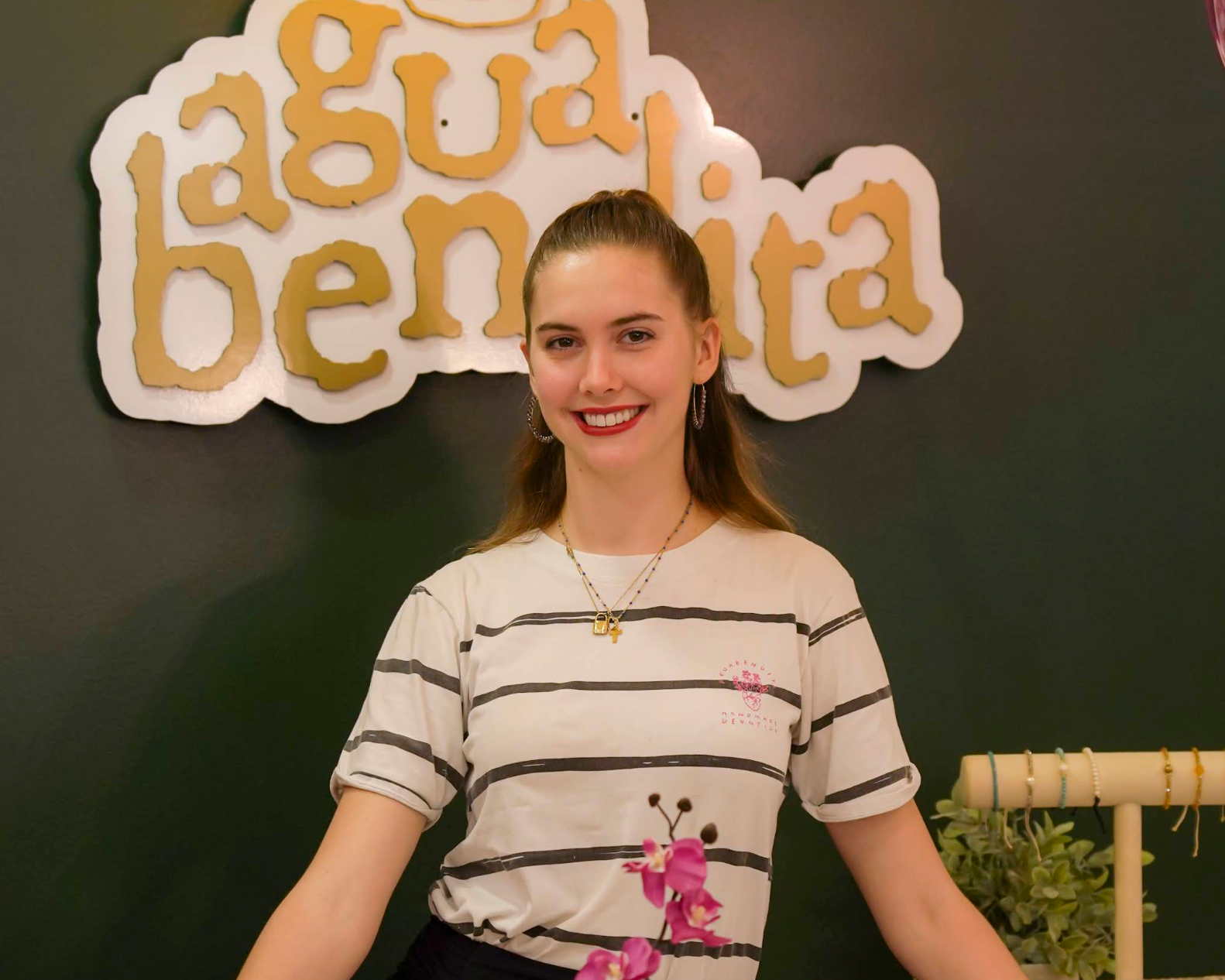 Woman standing behind a counter with 'agua bendita' sign in the background